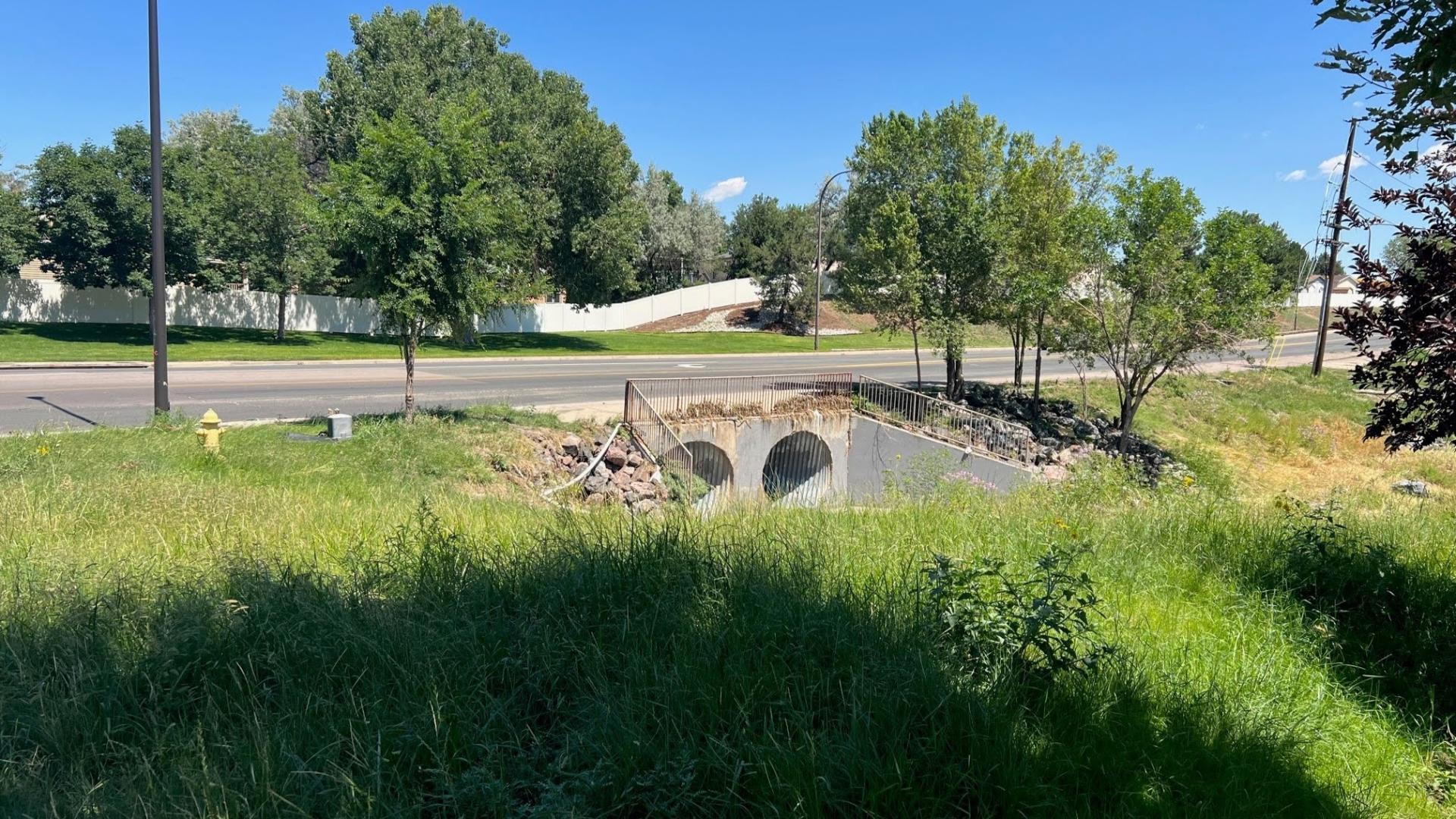 Dry stormwater outlet structure surrounded by green grass on a sunny day