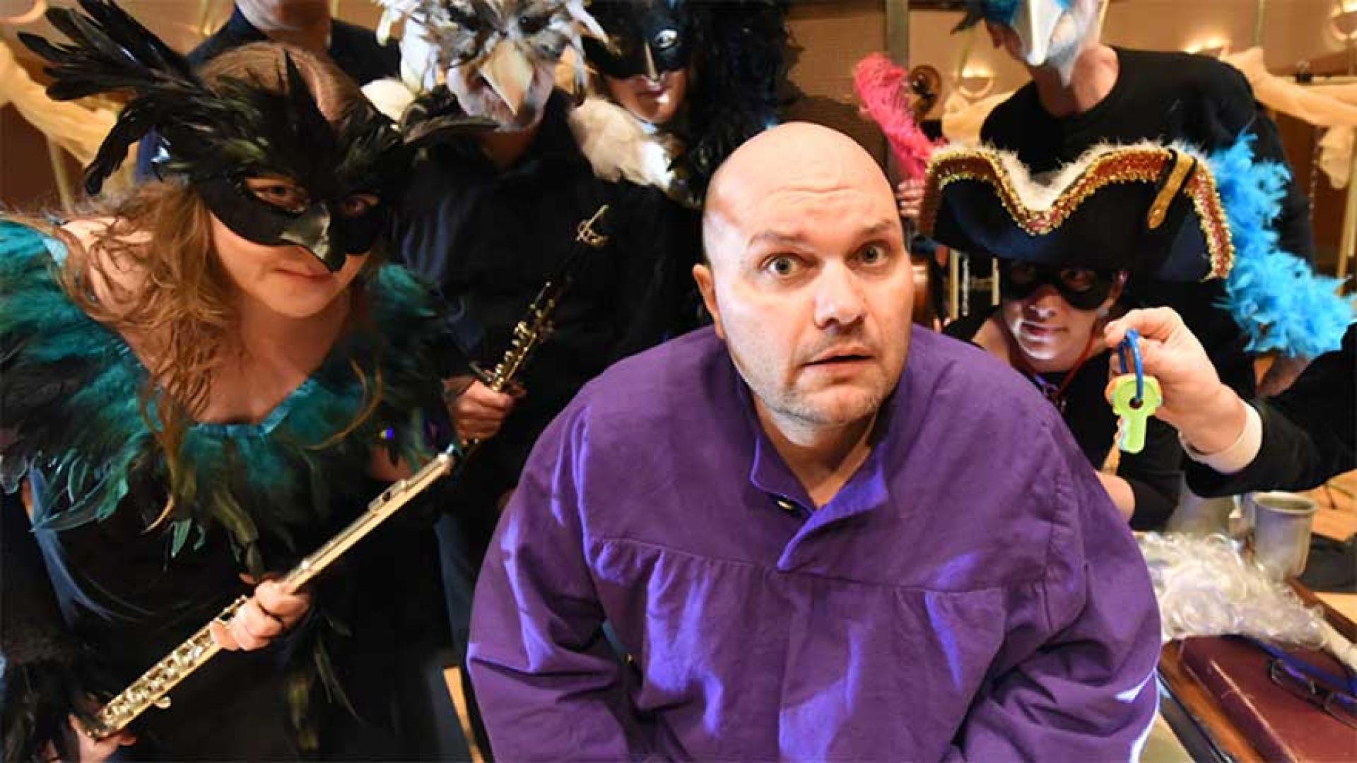Actor in purple shirt surrounded by masked actors.