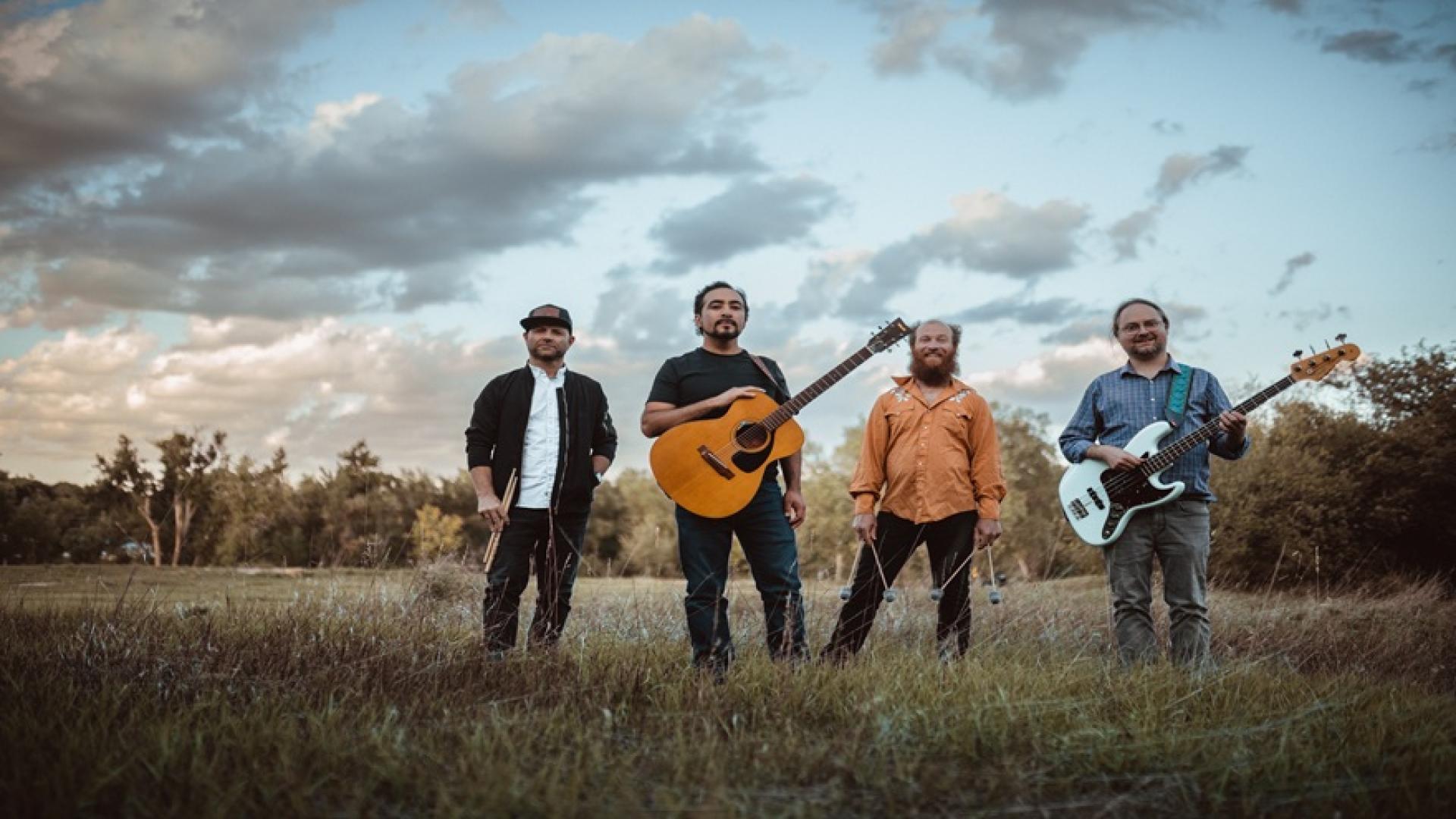 Four male musicians standing with instruments outdoors