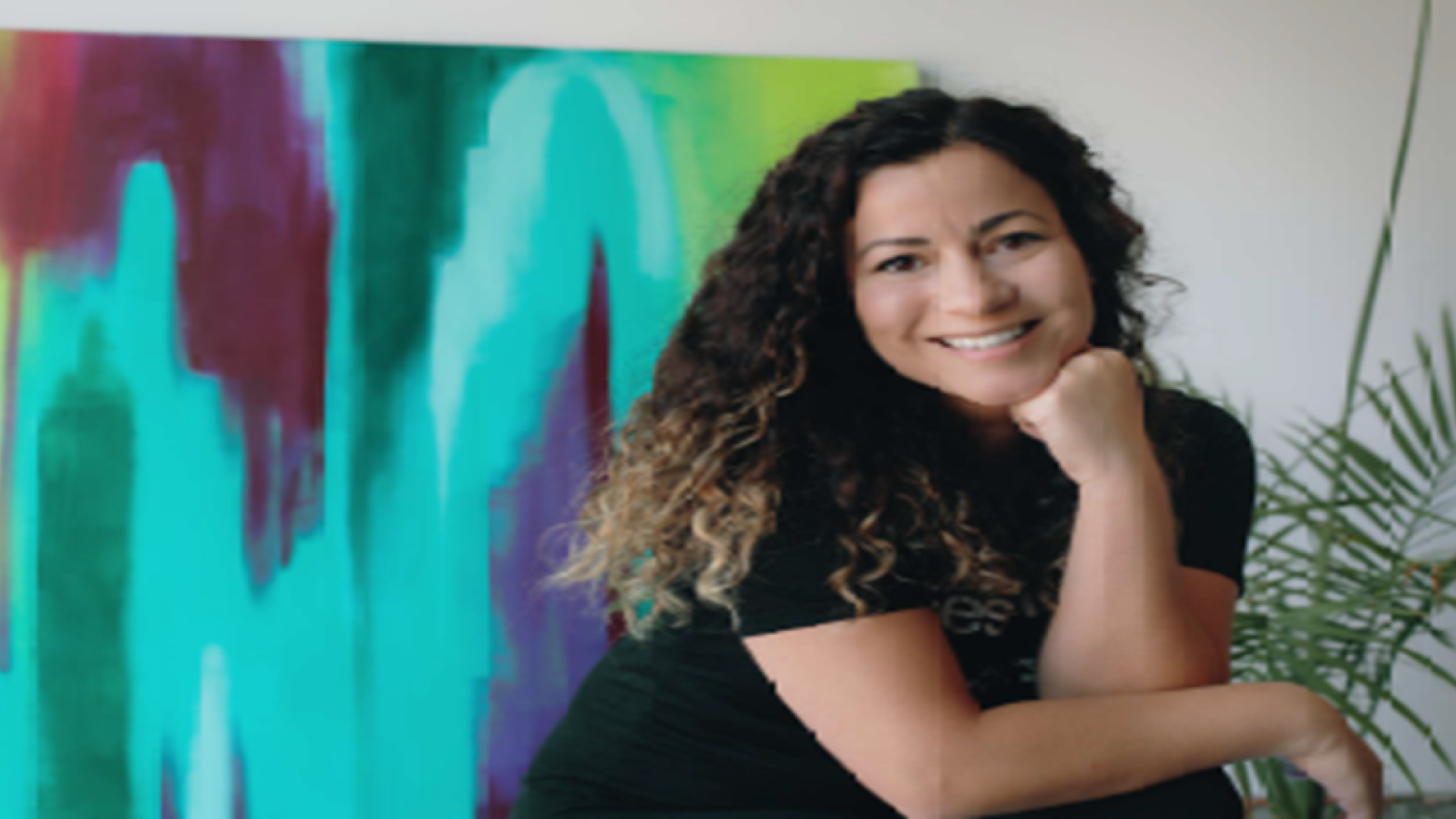 Latina artist seated in front of multicolor painting on wall