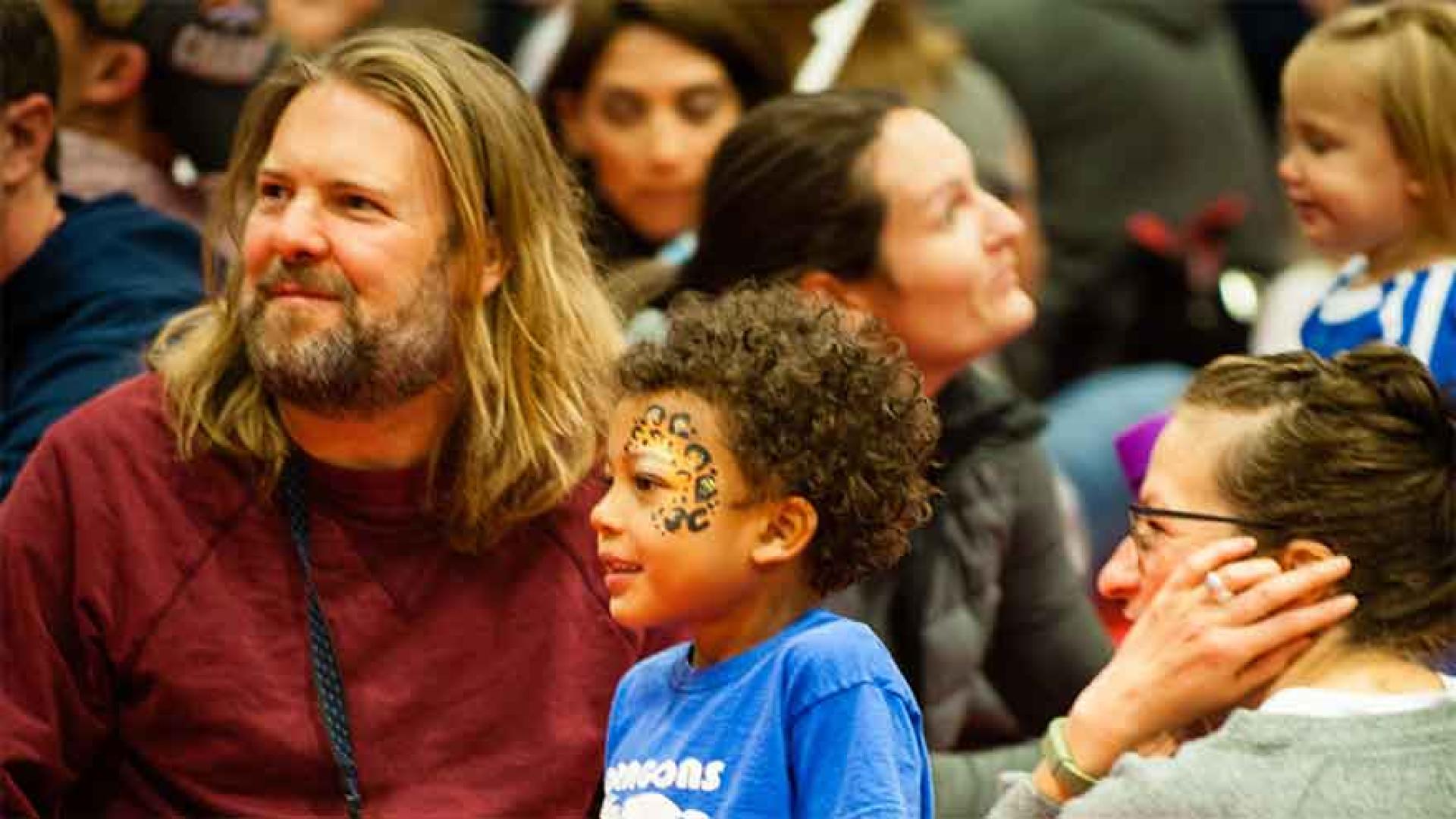 Young boy and adults in a crowd looking to the stage.