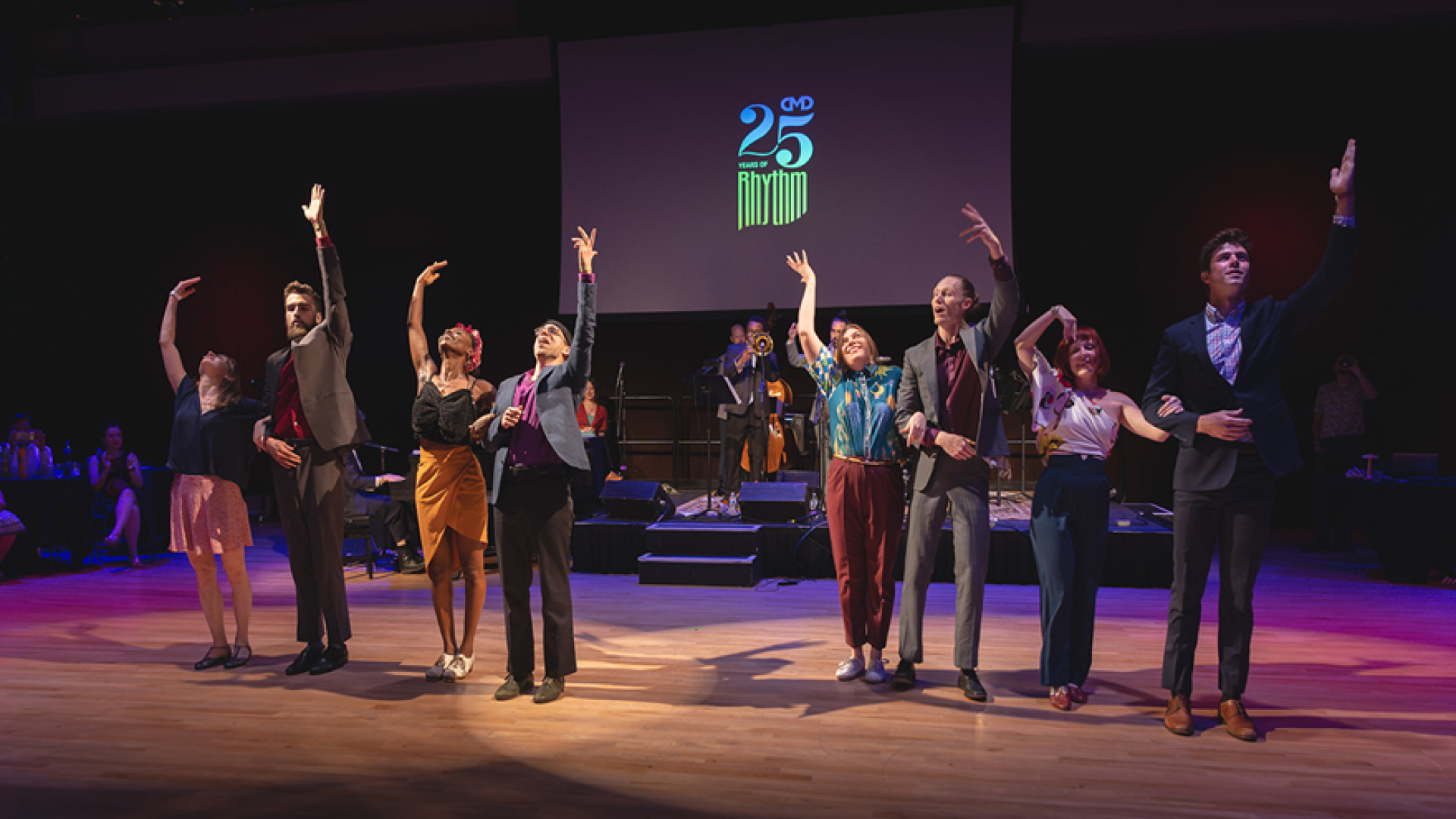 Eight adult dancers on stage waving to audience