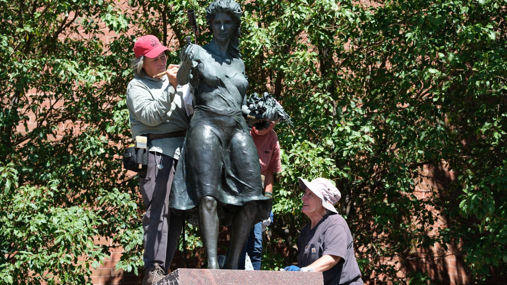 Three women work on cleaning a sculpture of a woman.