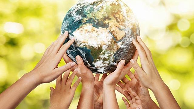 Hands holding up a small globe of the earth with blurred trees in the background.