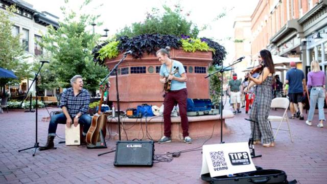 Three musicians performing outside on guitars and violin.