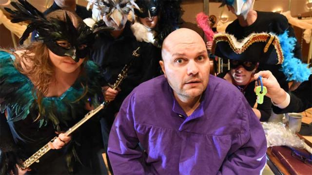 Actor in purple shirt surrounded by masked actors.