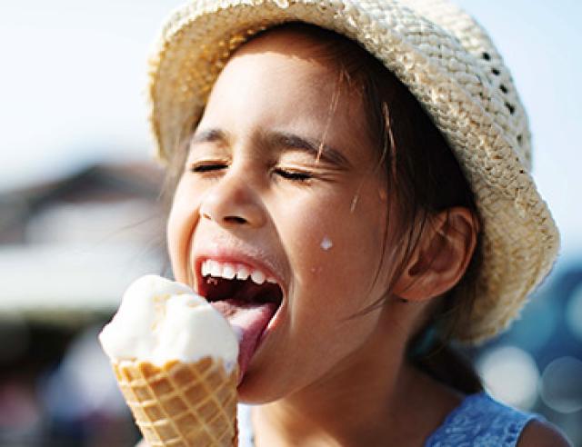 Little girl in a hat eating an ice cream cone.
