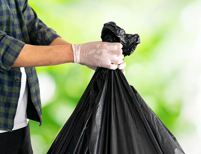 Person wearing white latex gloves and holding a black trash bag.