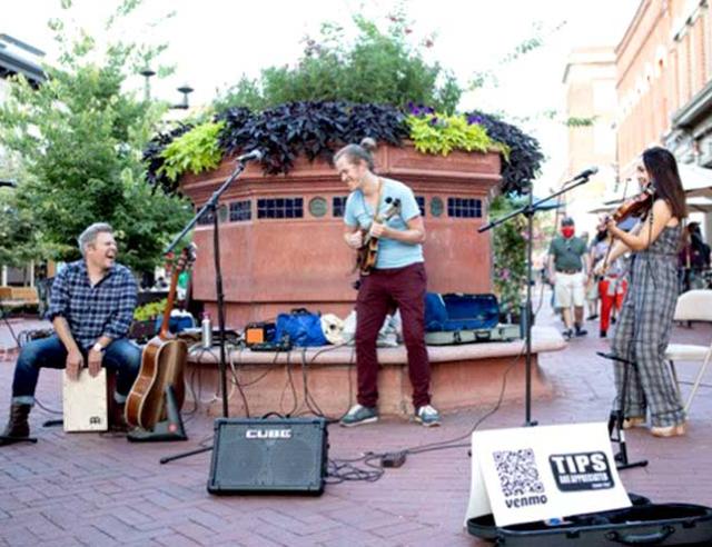 Three musicians performing outside on guitars and violin.