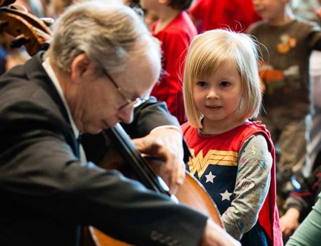 Young girl watching old man playing the cello.