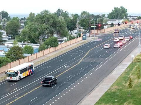 An isometric view of a section of Colorado Boulevard with two lanes in each direction, a center turn lane, bicycle lanes on both sides, and a right turn lane at the signalized intersection in the distance. Dashed lines mark parts of the bicycle lane, indicating the mixing zone where vehicles must merge through the bicycle lanes to reach the right turn lane. Traffic, including a city bus and several cars, drive by or queue at the traffic light.
